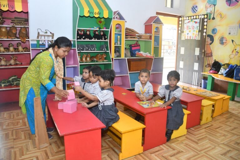 Teacher helping nursery children stack building blocks